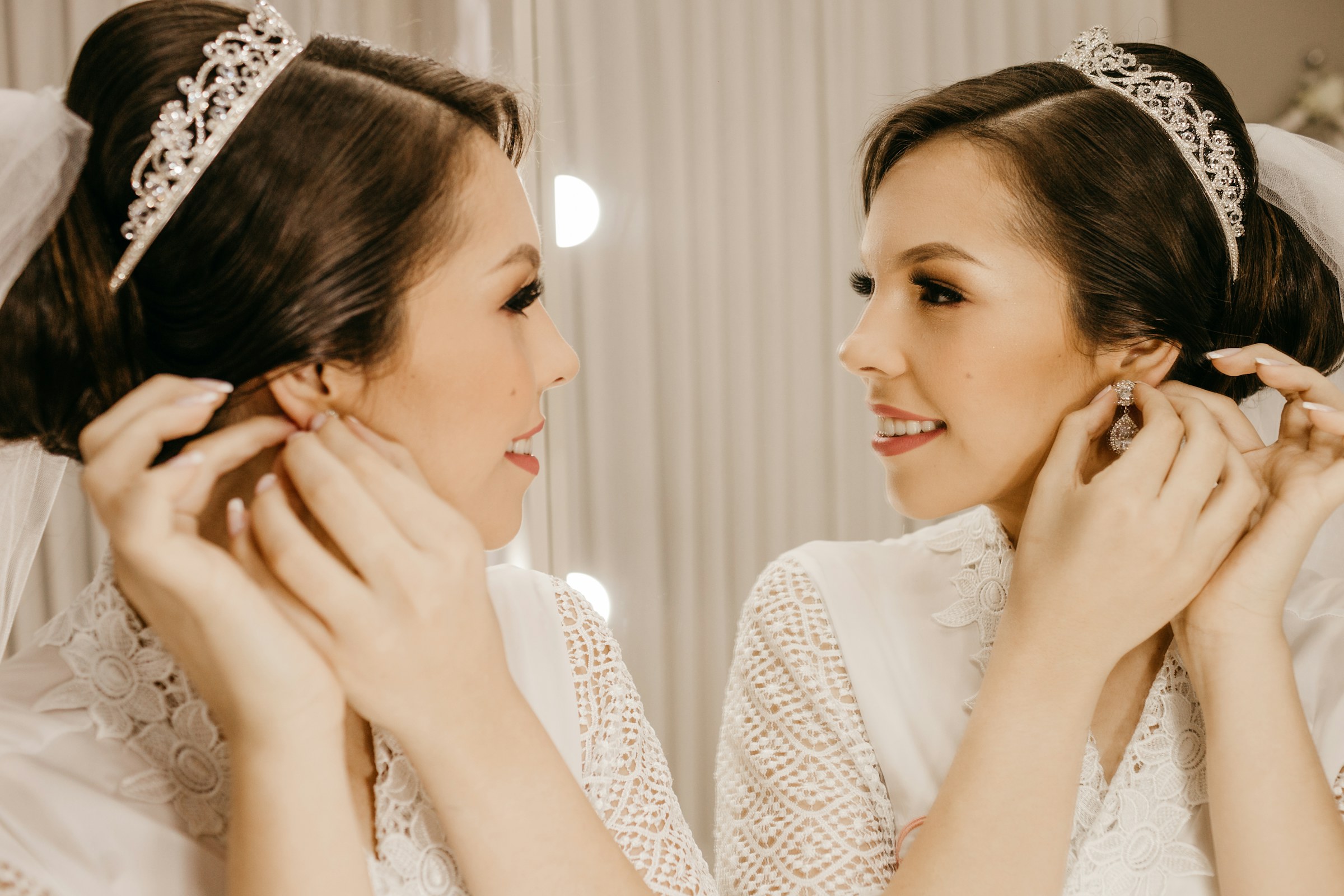 A bride fastening her earrings in front of the mirror